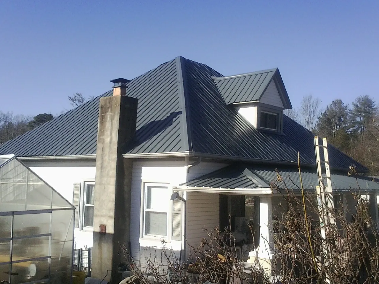 Dark blue standing seam metal roof on a white farmhouse with dormer — Slate & Tile Roof Repair by Roofing Brothers in Vale