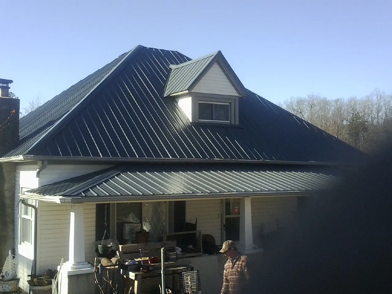 Dark blue standing seam metal roof with a dormer above a front porch in Vale
