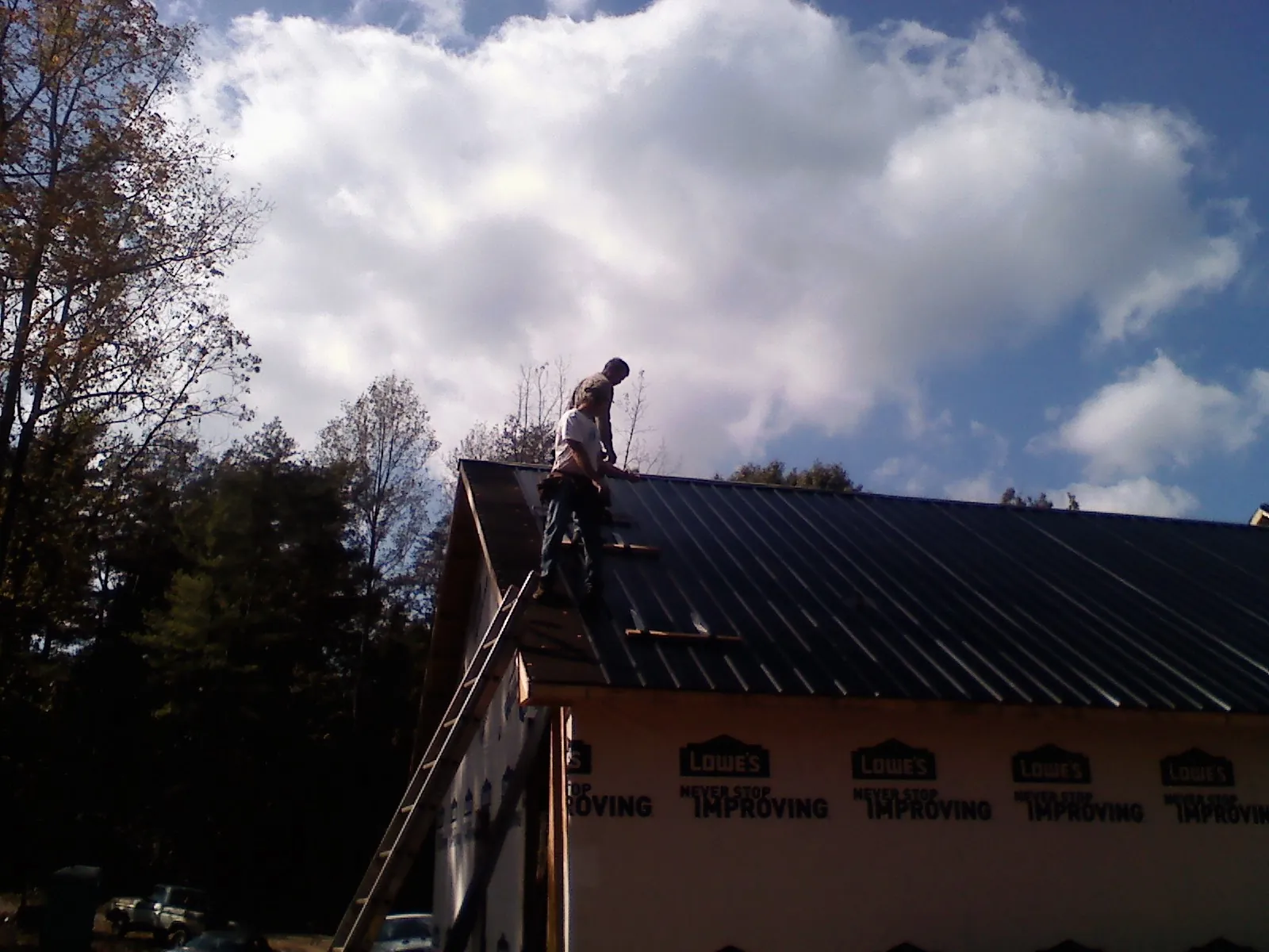 Roofer fastening dark metal panels high against a cloudy sky, from a Roof Inspection job in Vale